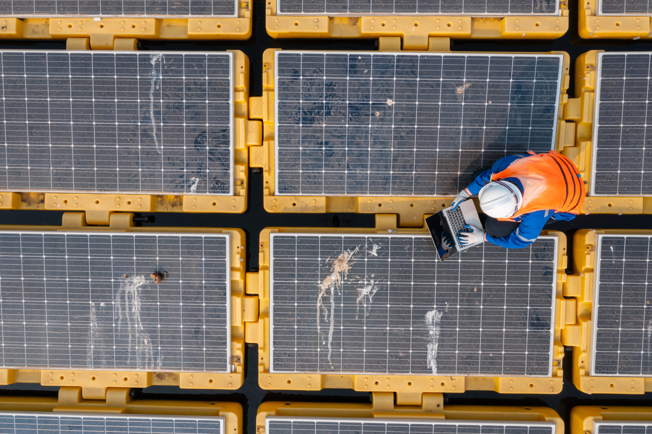 An engineer stands on a floating solar panel platform, using a laptop to assess the system's performance in a water-based installation.