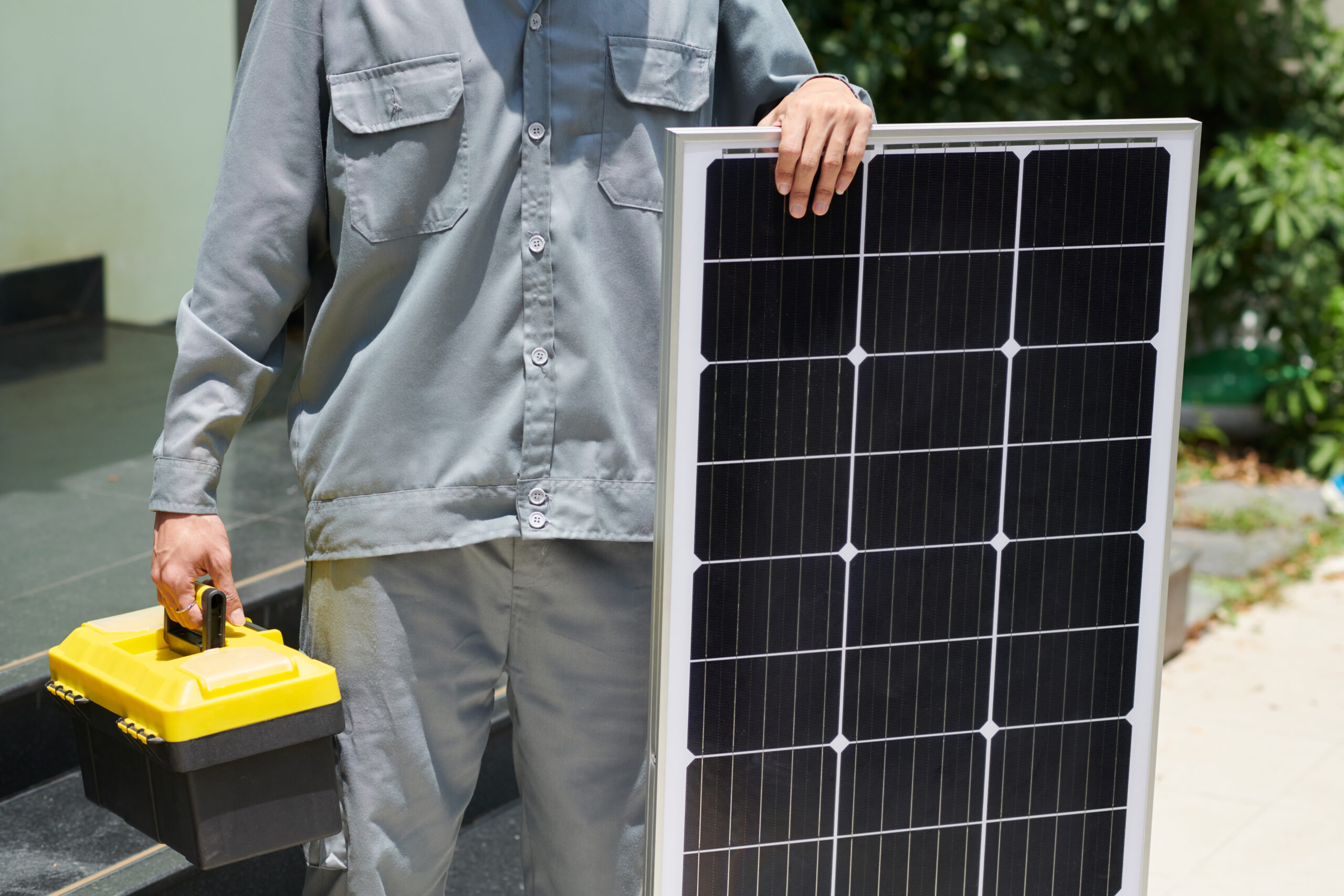 Croped image of installer with toolbox standing next to solar panel
